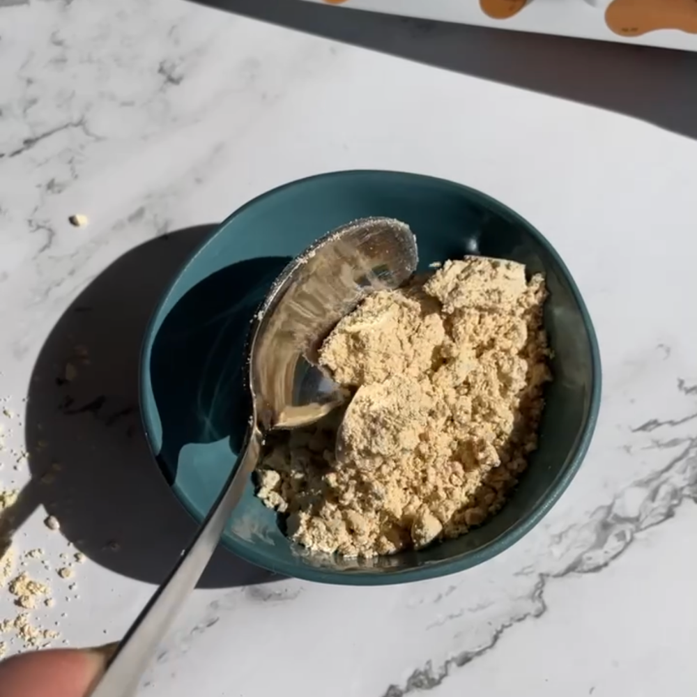 Peanut butter powder in a small, blue bowl with a silver spoon.