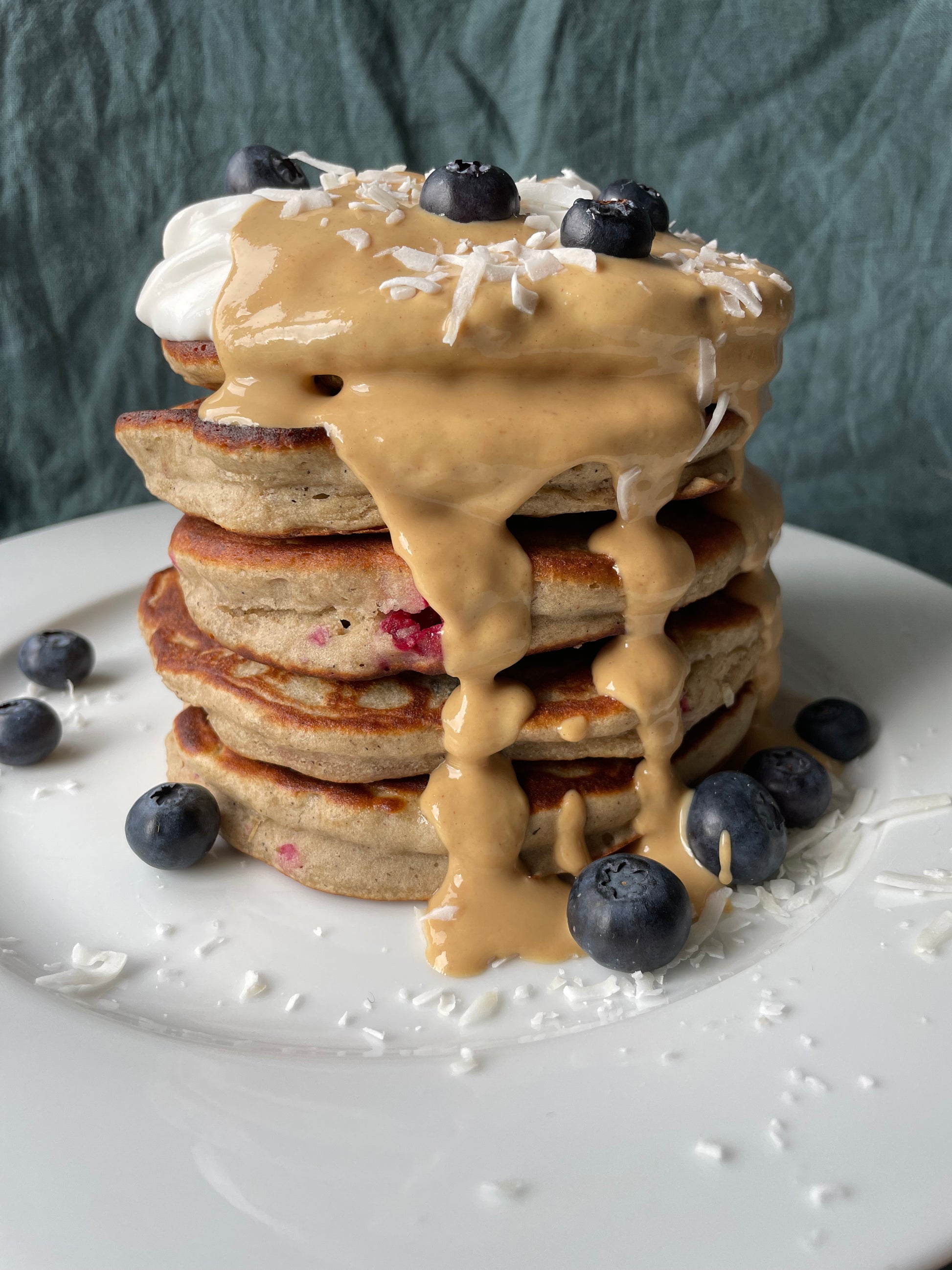 Peanut Butter protein pancakes on a plate topped with extra peanut butter powder, coconut yoghurt and blueberries. 